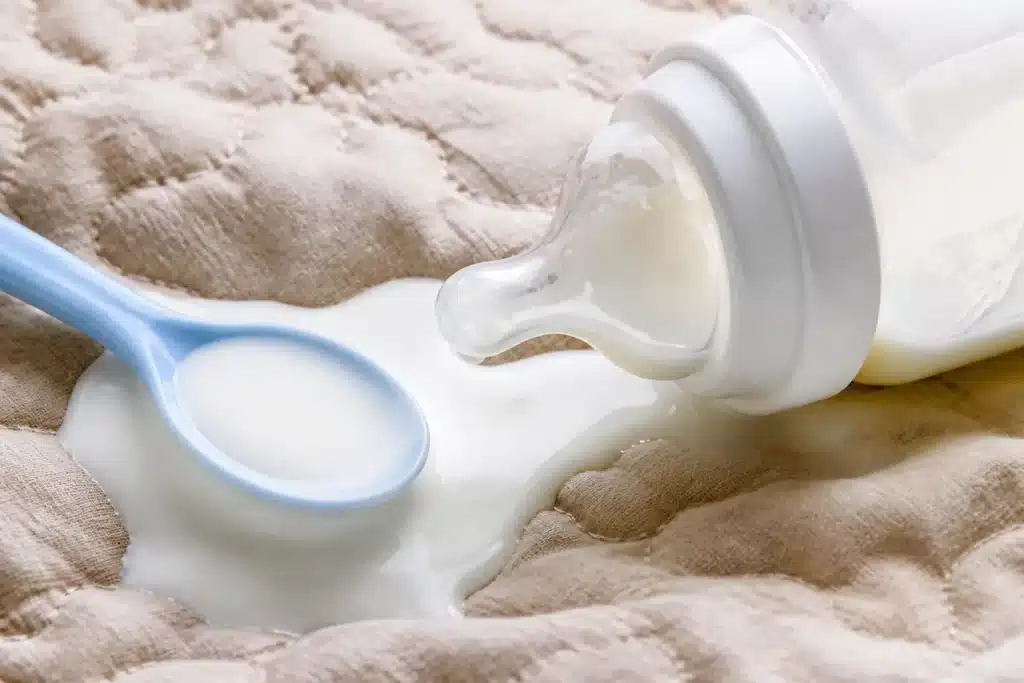 Biberon et cuillere en contact avec lait frais blanc