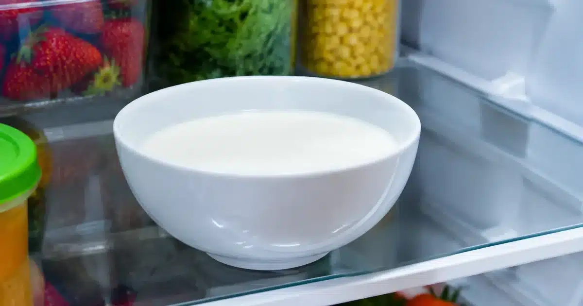 Bol blanc rempli de lait repose sur etagere refrigerateur ouvert