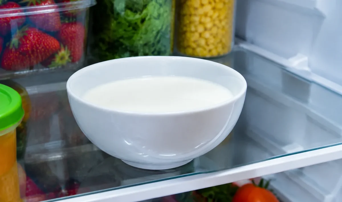 Bol blanc rempli de lait repose sur etagere refrigerateur ouvert