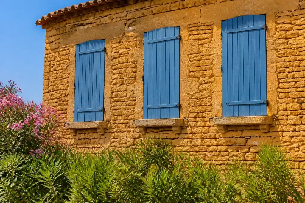 Facade provencale en pierre ocre avec volets bleus fermés