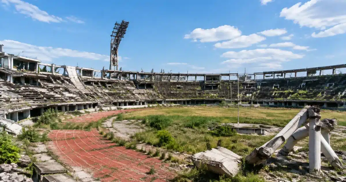 Stades olympiques en ruine, structures beton delabrees, gradins vides et colonnes effondrees