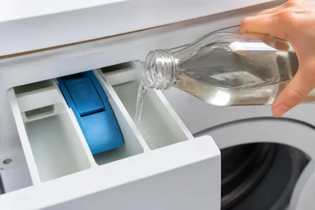 Bouteille vinaigre versée dans compartiment lave-linge blanc