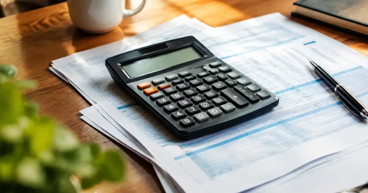 Main tenant une calculatrice posée sur des bulletins de salaire