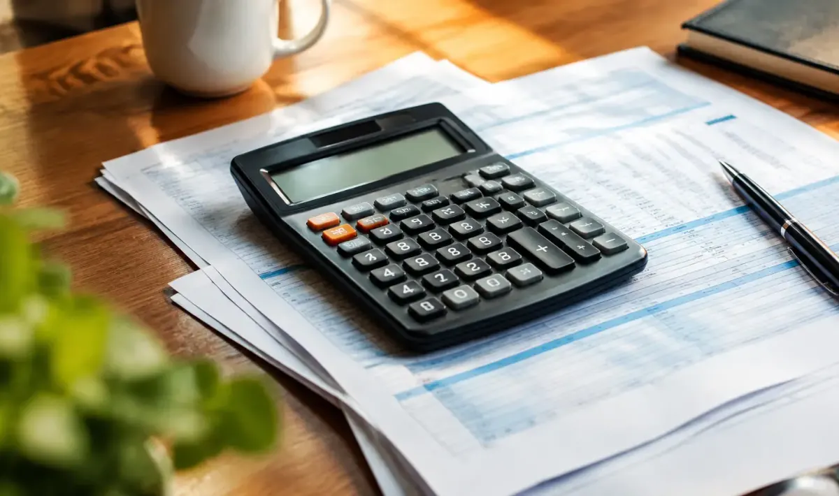 Main tenant une calculatrice posée sur des bulletins de salaire