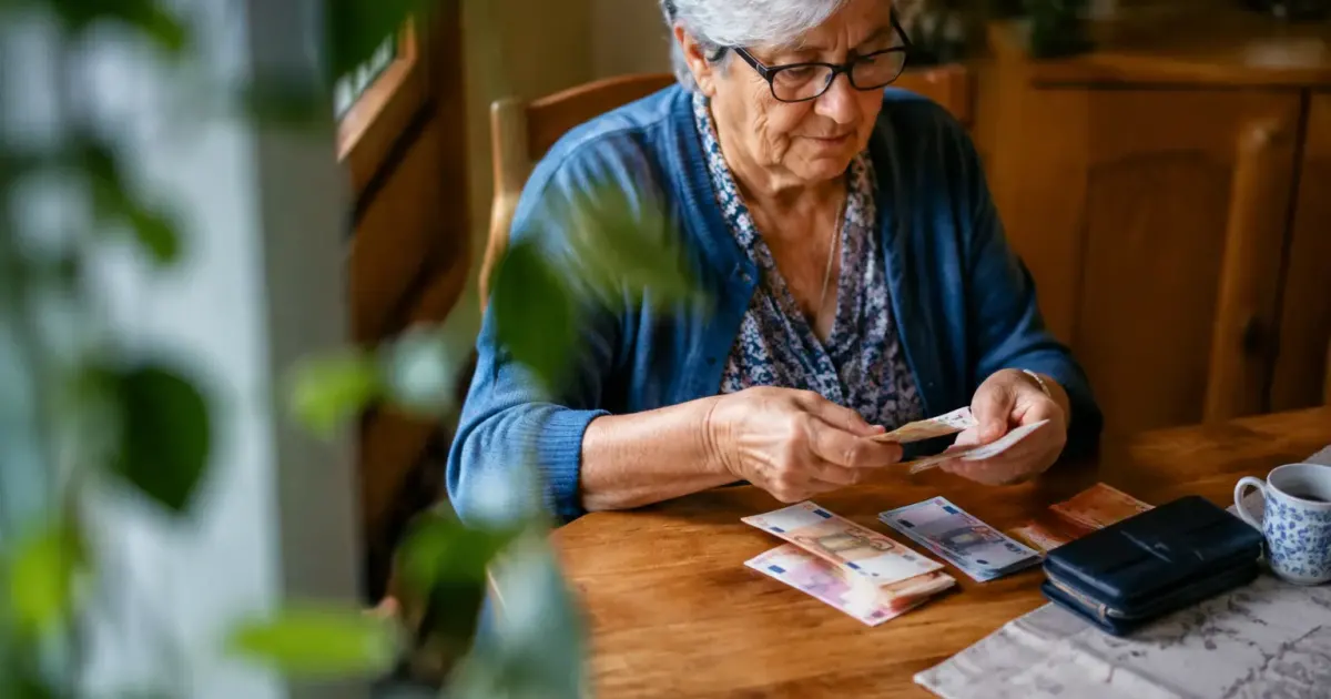 Femme agee assise comptant billets sur table en bois