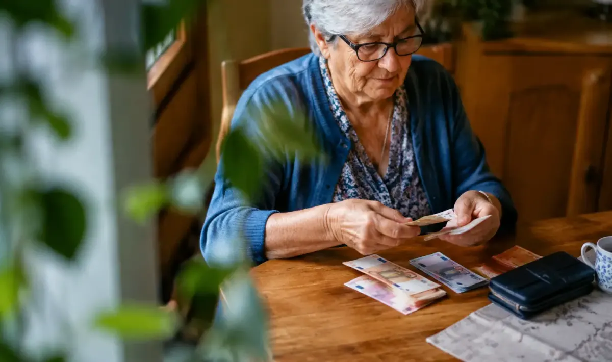Femme agee assise comptant billets sur table en bois