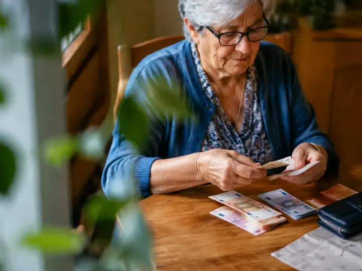 Femme agee assise comptant billets sur table en bois