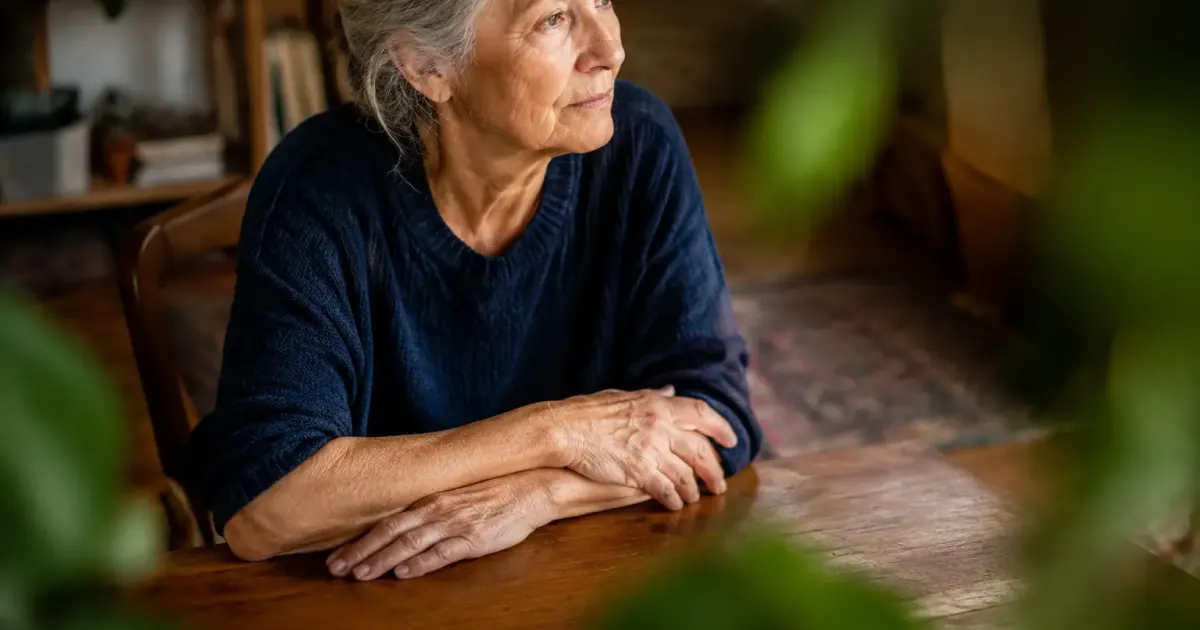 Femme agee assise, mains croisees sur une table