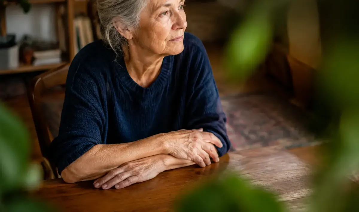 Femme agee assise, mains croisees sur une table
