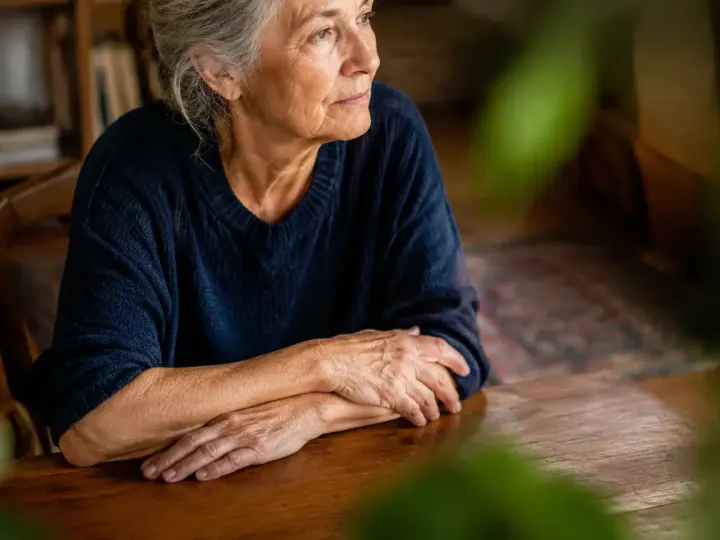 Femme agee assise, mains croisees sur une table