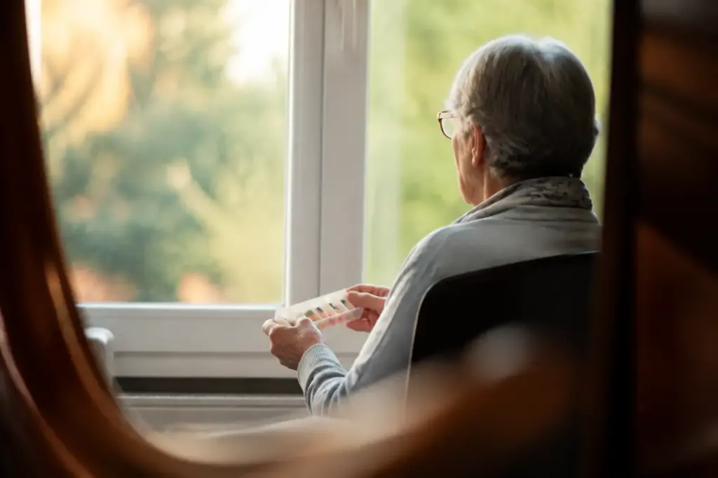 Femme assise devant la fenetre tenant un pilulier