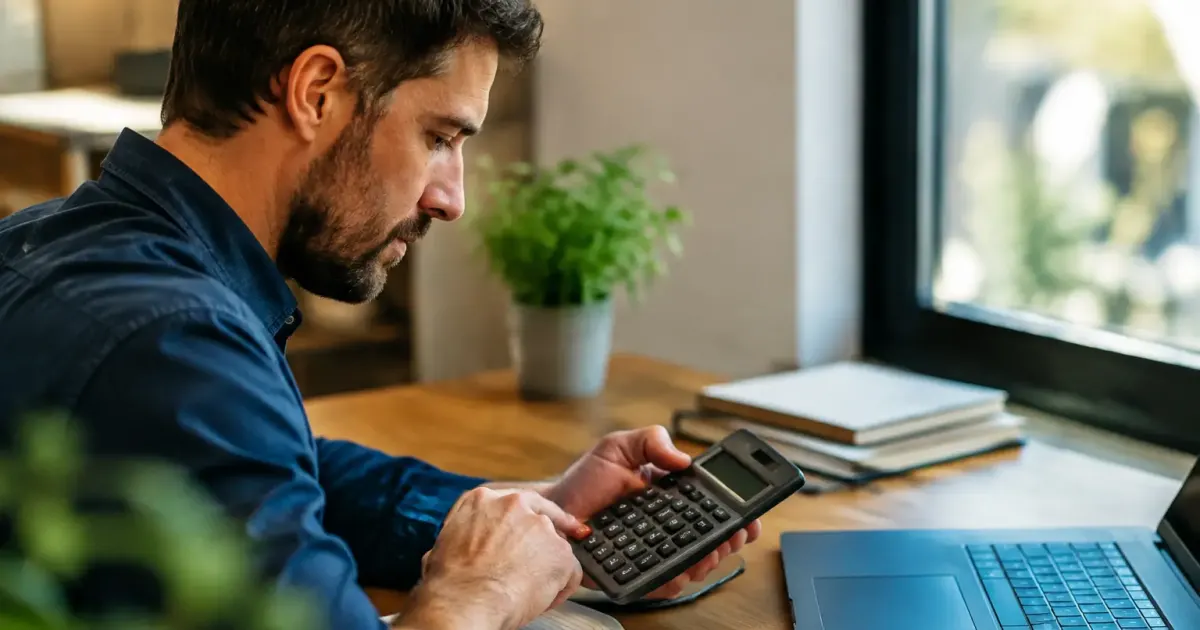 Homme assis a un bureau tenant une calculatrice