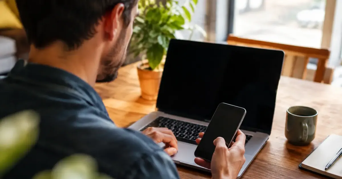 Homme assis tenant un telephone devant un ordinateur portable