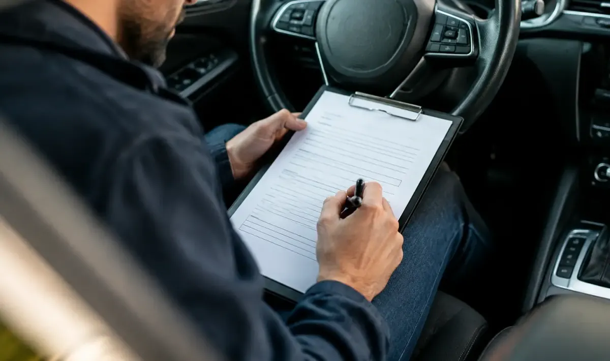 Un homme assis au volant signe un formulaire papier