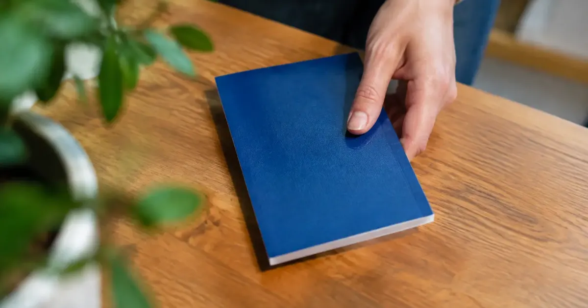 Main posant un carnet bancaire bleu sur table