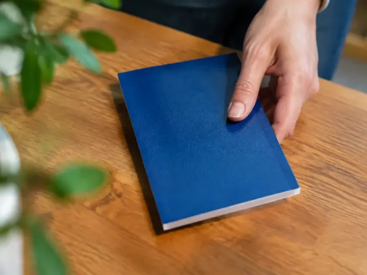 Main posant un carnet bancaire bleu sur table