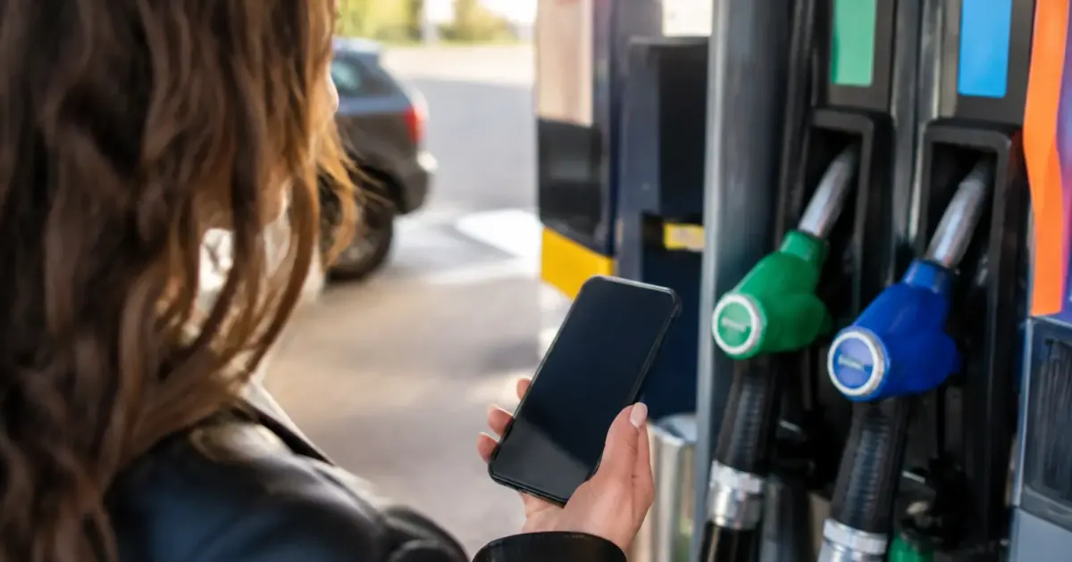 Main tenant un smartphone devant une pompe essence