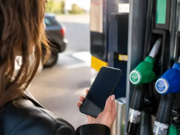 Main tenant un smartphone devant une pompe essence