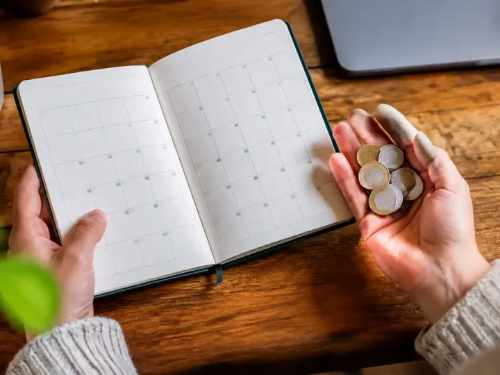 Une main tient un calendrier ouvert et des monnaies