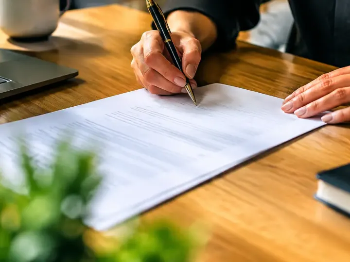 Mains signant un document sur un bureau en bois