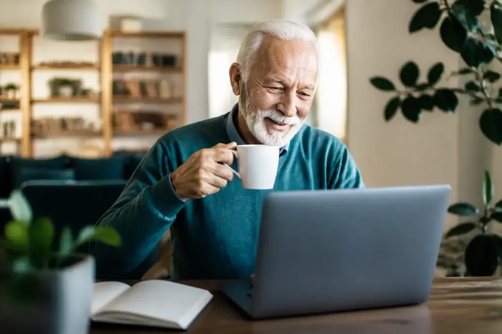 Senior souriant avec tasse de cafe devant ordinateur portable