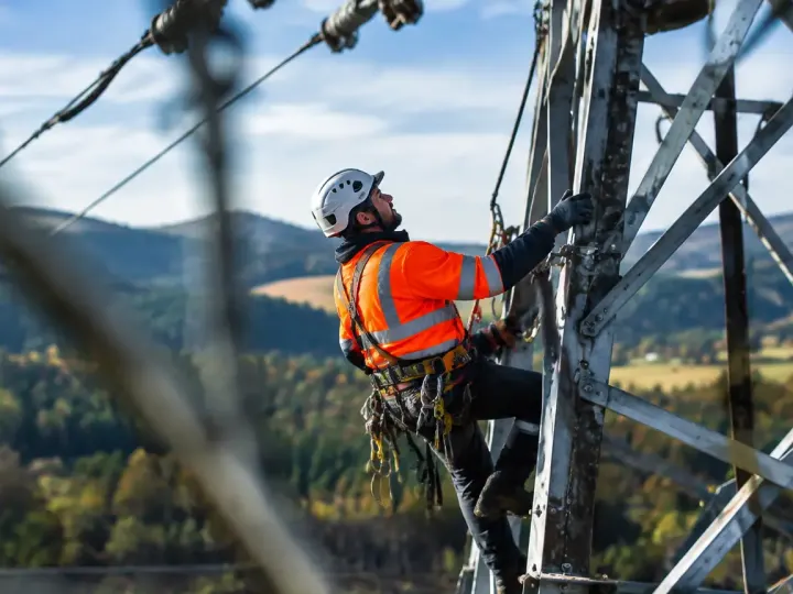 Technicien en gilet orange grimpe sur un pylone
